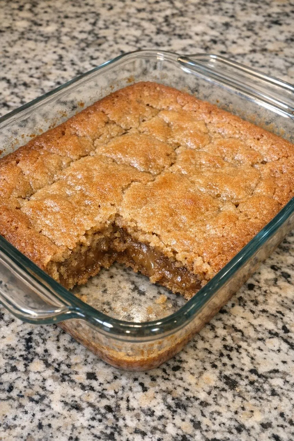 Freshly baked blondies in an eight-inch glass baking dish with one square cut out showing the gooey center.