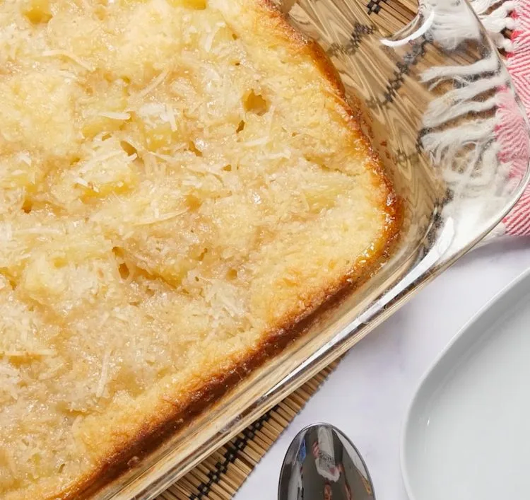 Baked pineapple coconut cobbler with a golden coconut crust in a clear glass casserole dish.