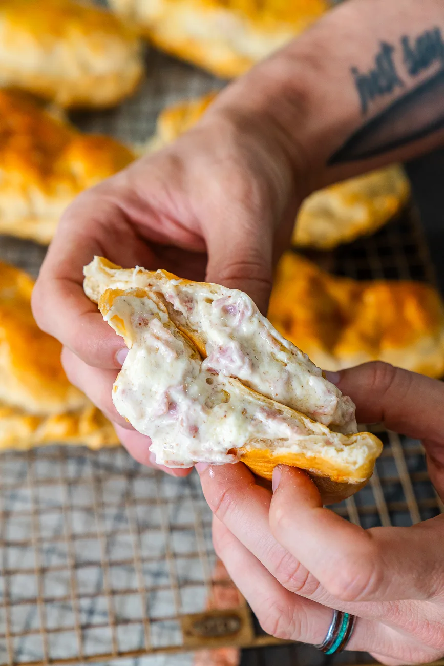 A baked hand pie pulled apart by hand to show the creamy ham and melted Swiss cheese filling inside the pastry crust.