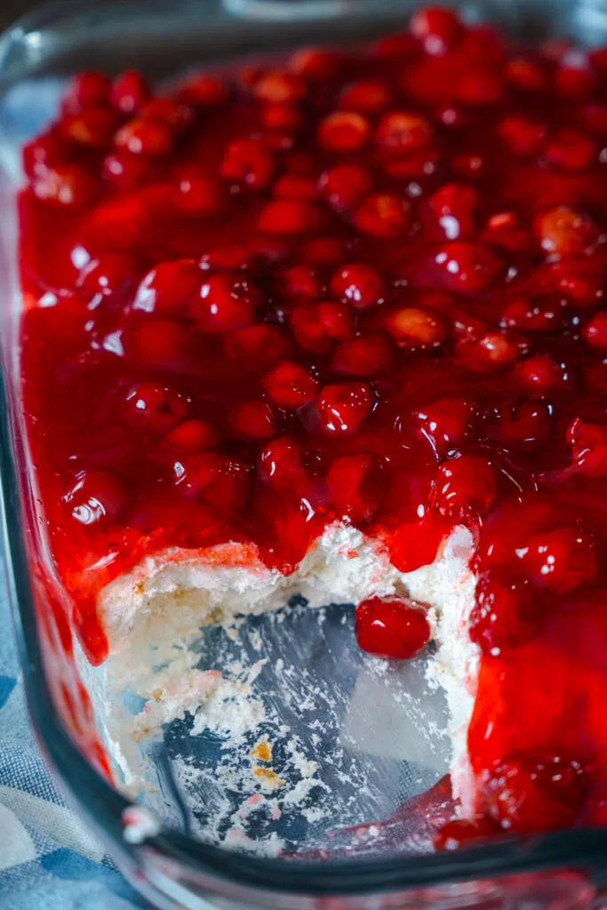 A 9x13-inch glass baking dish of Cherries in the Snow with a corner portion scooped out, resting on a blue-checked cloth.